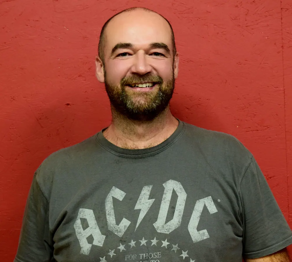 Portrait souriant du chef de chœur devant un mur rouge